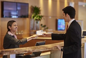 Un comptoir d’accueil où une femme tend une carte à un homme.