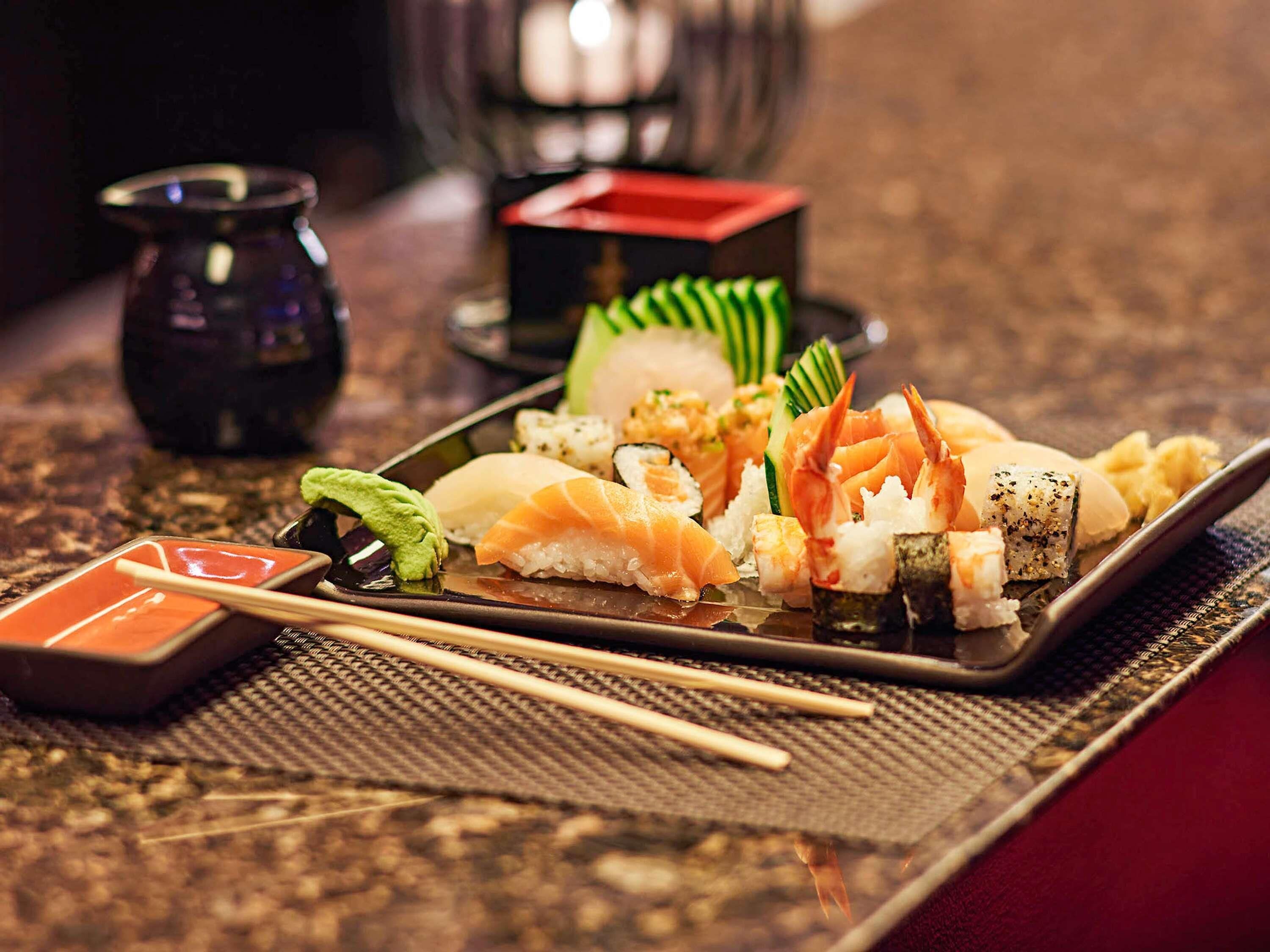 Un plato de sushi con diferentes tipos de sushi, un tazón pequeño de salsa de soja y palillos sobre una mesa.
