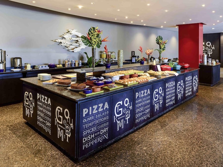 A buffet area with a variety of food options including pizza, olives, salads, and dishes with spices and cheese.