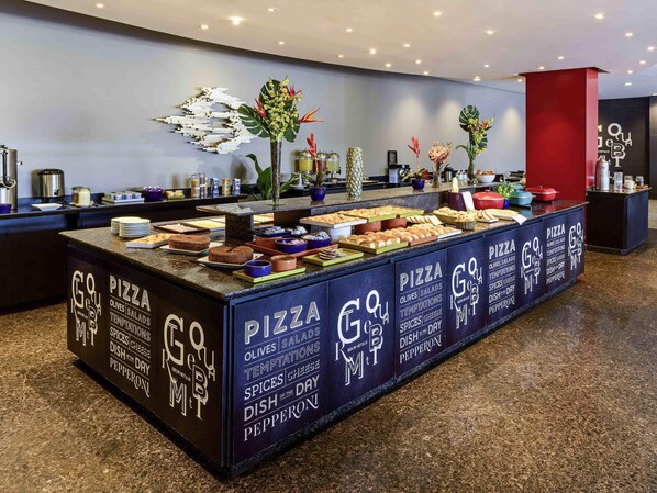 Een buffetgedeelte met diverse gerechten, waaronder pizza, olijven, salades en schotels met specerijen en kaas.
