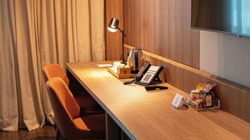 A hotel room with a wooden desk, a telephone, a lamp, and a television mounted on the wall.