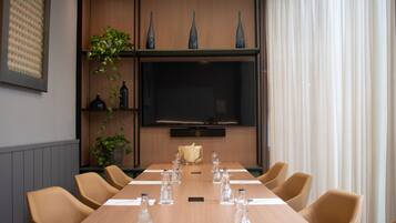 Una sala conferenze con un lungo tavolo, sedie, uno schermo televisivo e vasi decorativi.