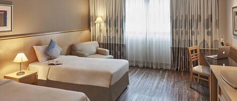 A hotel room with two beds, a desk, and a chair.