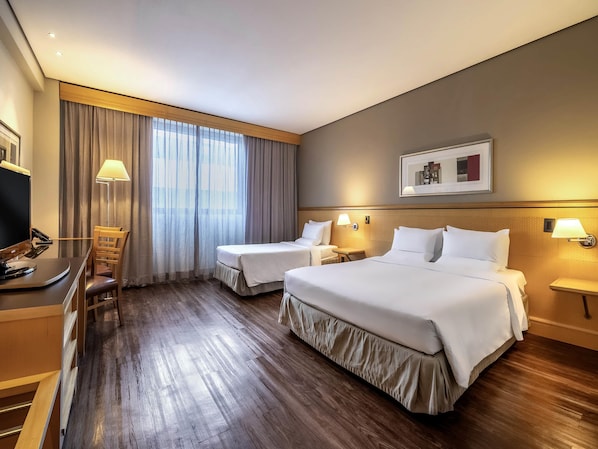 A hotel room with two beds, a desk with a computer, a chair, and a window with curtains.