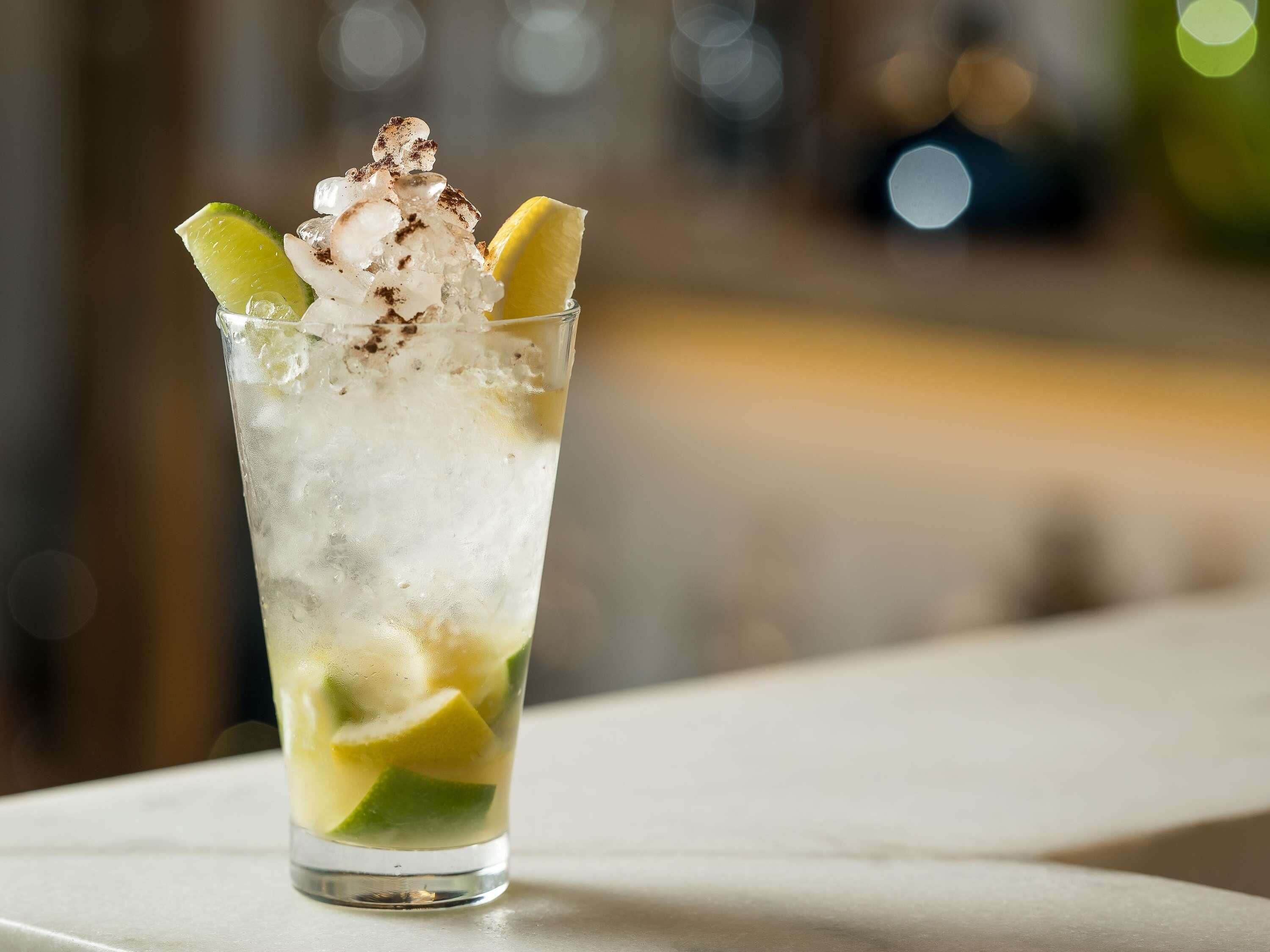 A glass of iced beverage with lime and mint, placed on a table.
