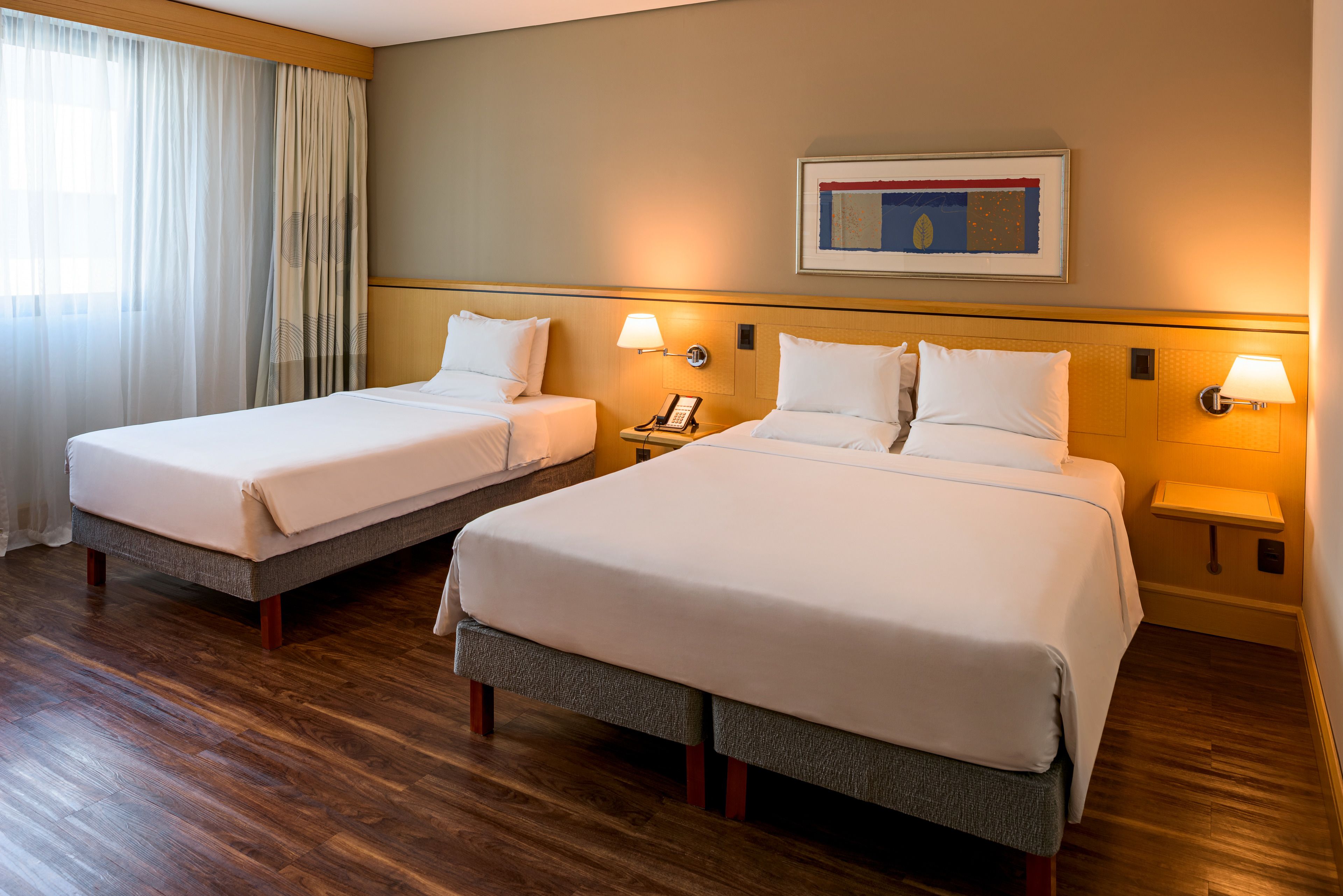 A hotel room with two beds, wooden flooring, and bedside lamps.