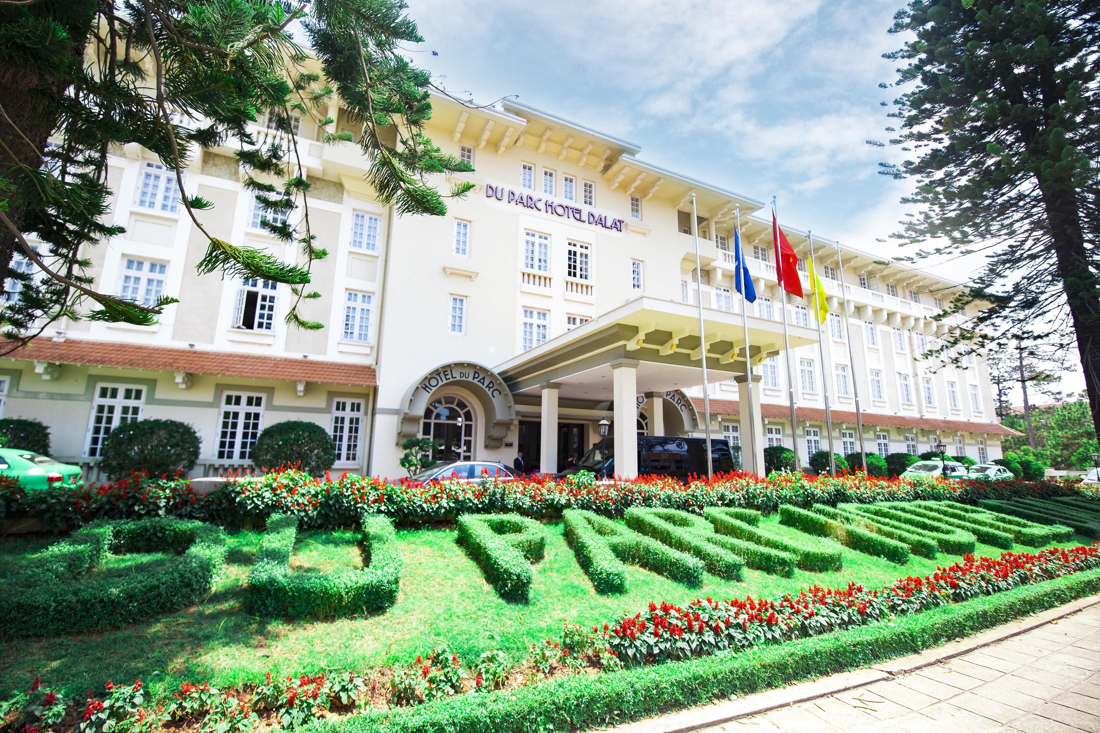 Das Du Parc Hotel Dalat mit gepflegtem Garten und mehreren Flaggen.