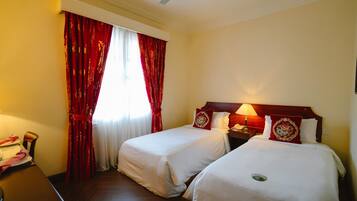 A hotel room with two beds, a desk, a chair, a lamp, and a ceiling fan.