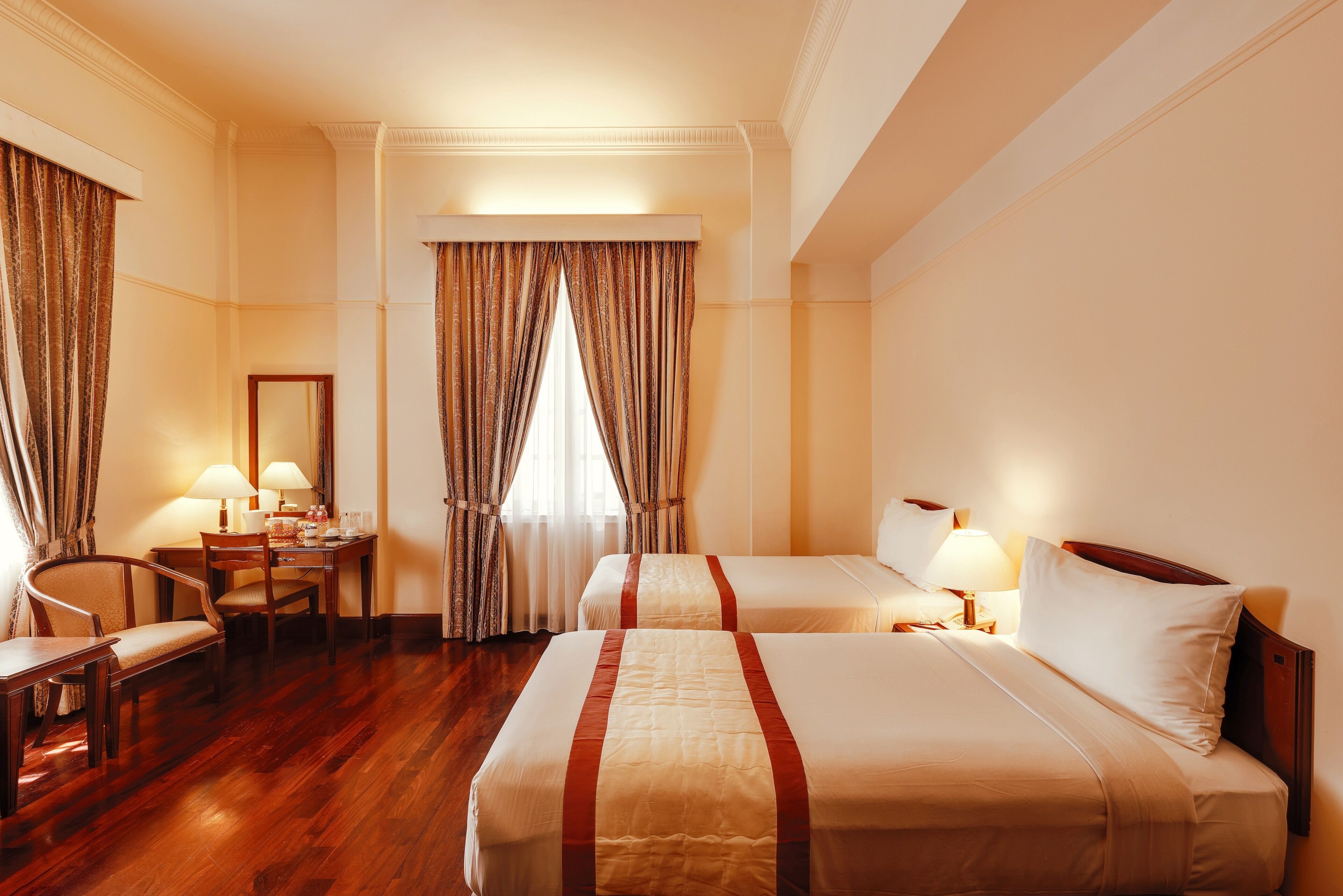 A hotel room with two beds, a desk, a chair, and a window with curtains.