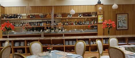 Un restaurante con área de bar, paneles de madera y una variedad de botellas y copas a la vista.