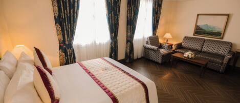 A hotel room with a bed, a sofa, a chair, a lamp, and a painting on the wall.