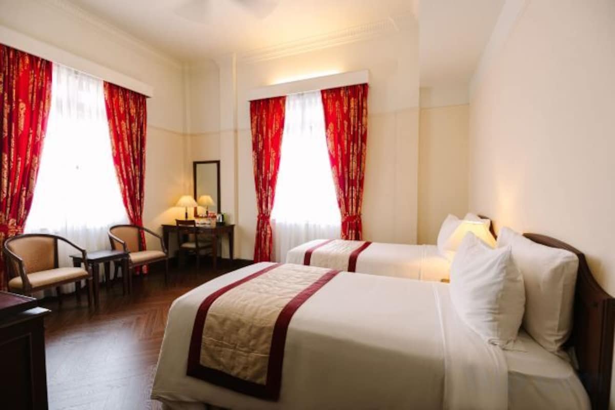 A hotel room with two beds, a desk, a chair, and red curtains.