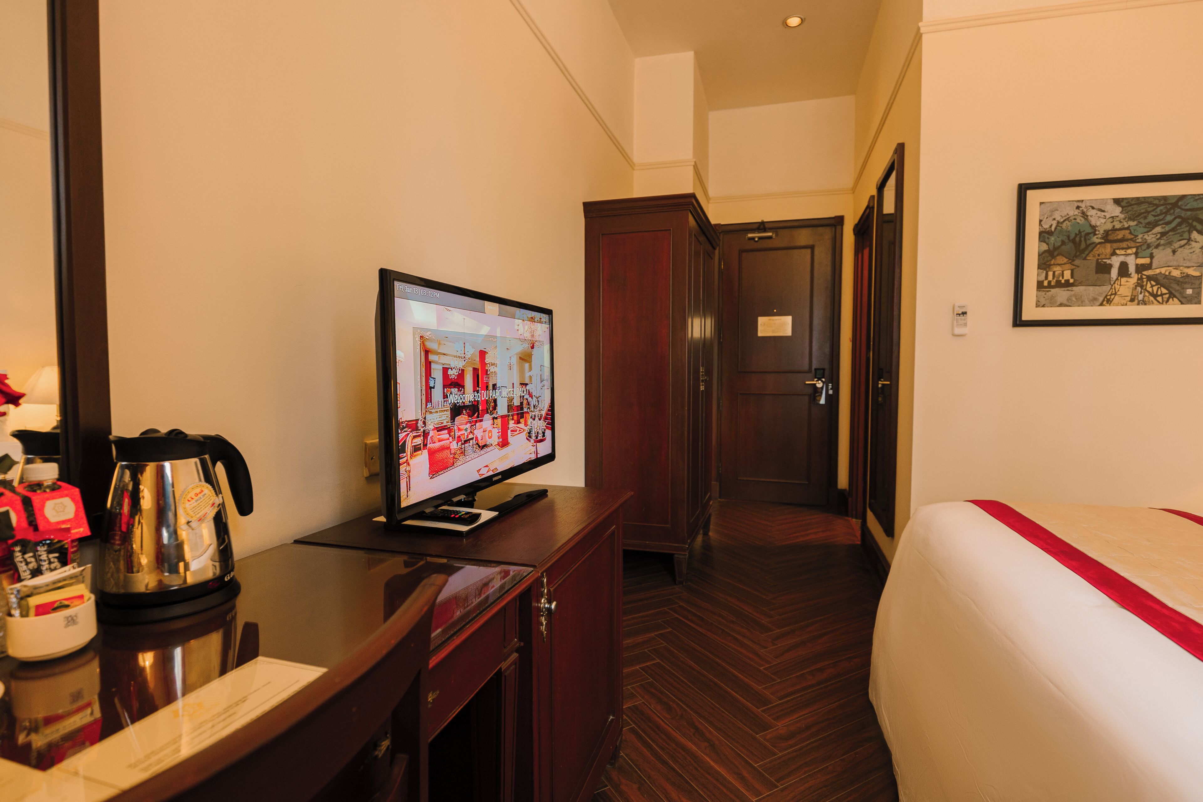 A hotel room with a bed, a television on a desk, a coffee maker, and a door leading to another room.