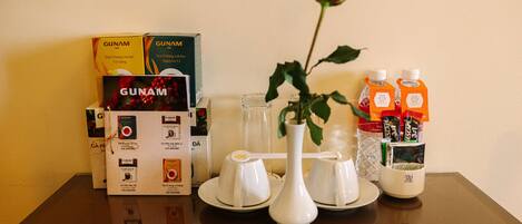 Una mesa con cajas de té GUNAM, un jarrón blanco con una rosa y dos botellas de jugo de naranja.