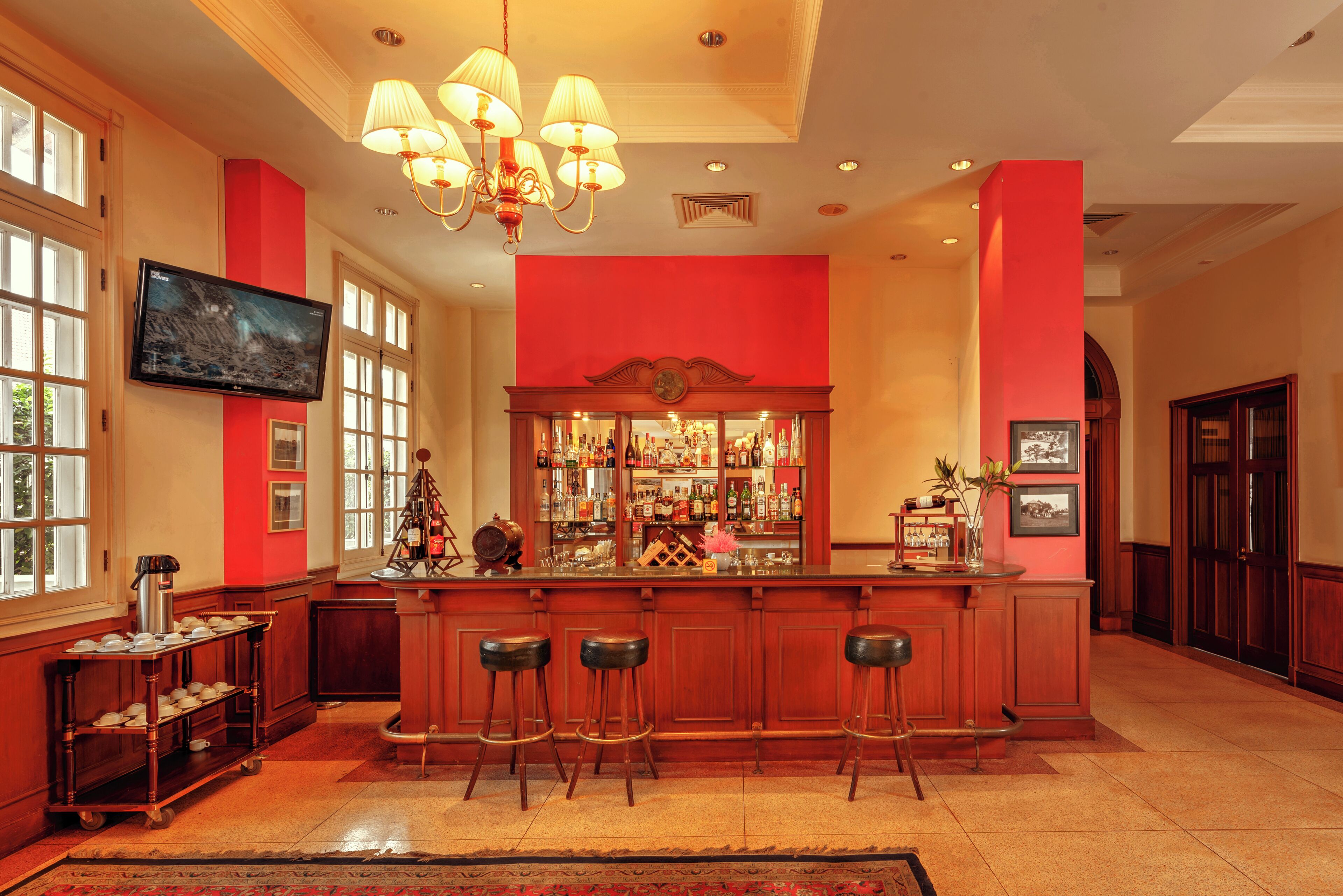 A bar area with a red accent wall, a television mounted above the bar, and a chandelier.