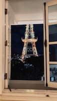 A view of the Eiffel Tower at night through an open window.