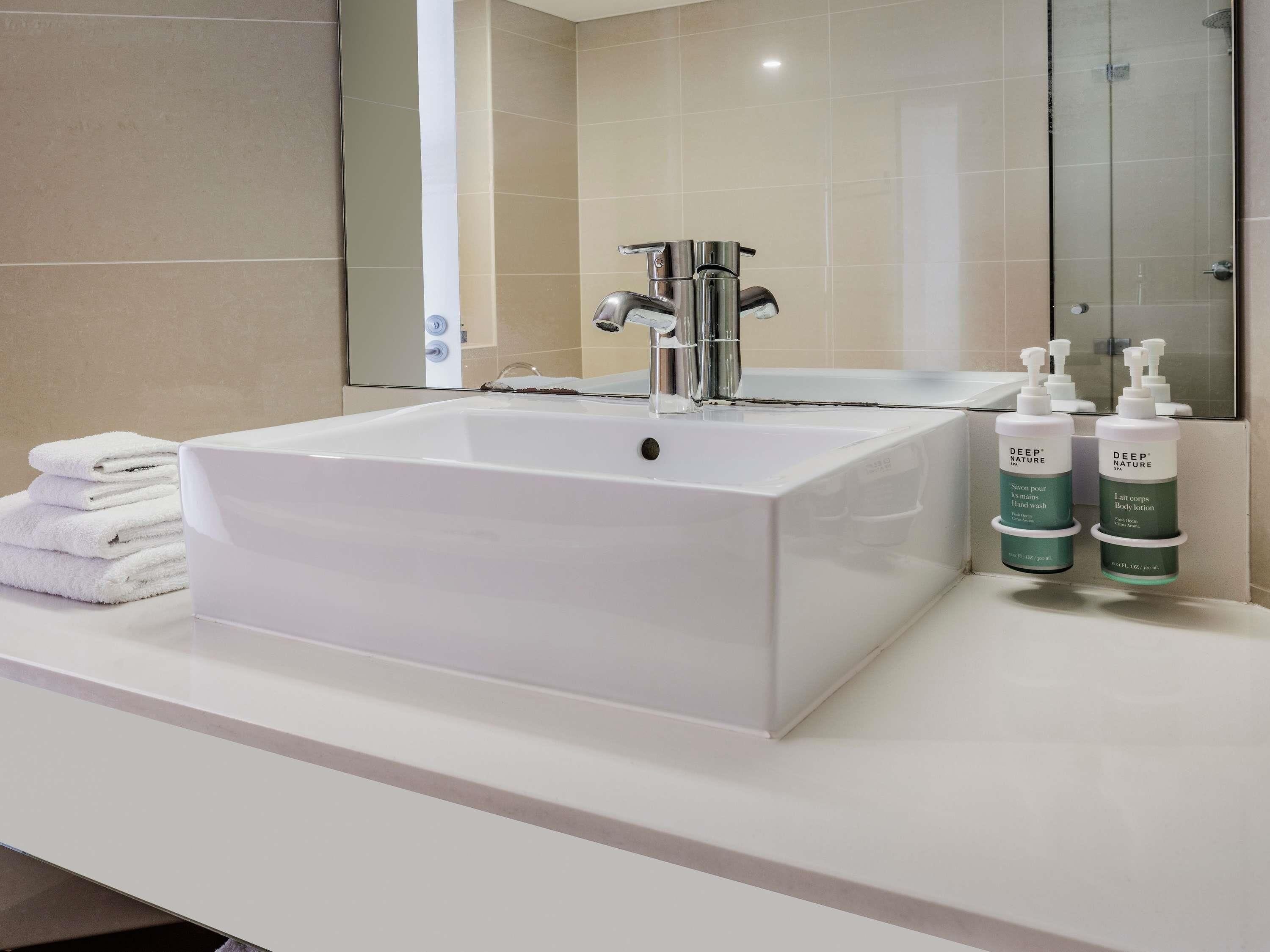 A bathroom with a white sink, a mirror, and two bottles of Deep Nature body lotion.