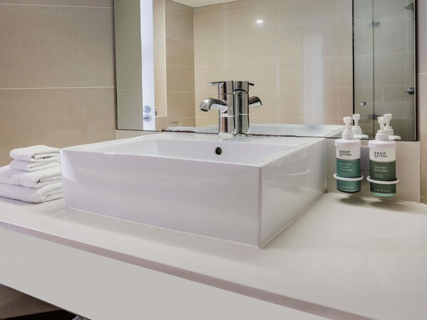 A bathroom with a white sink, a mirror, and two bottles of Deep Nature body lotion.