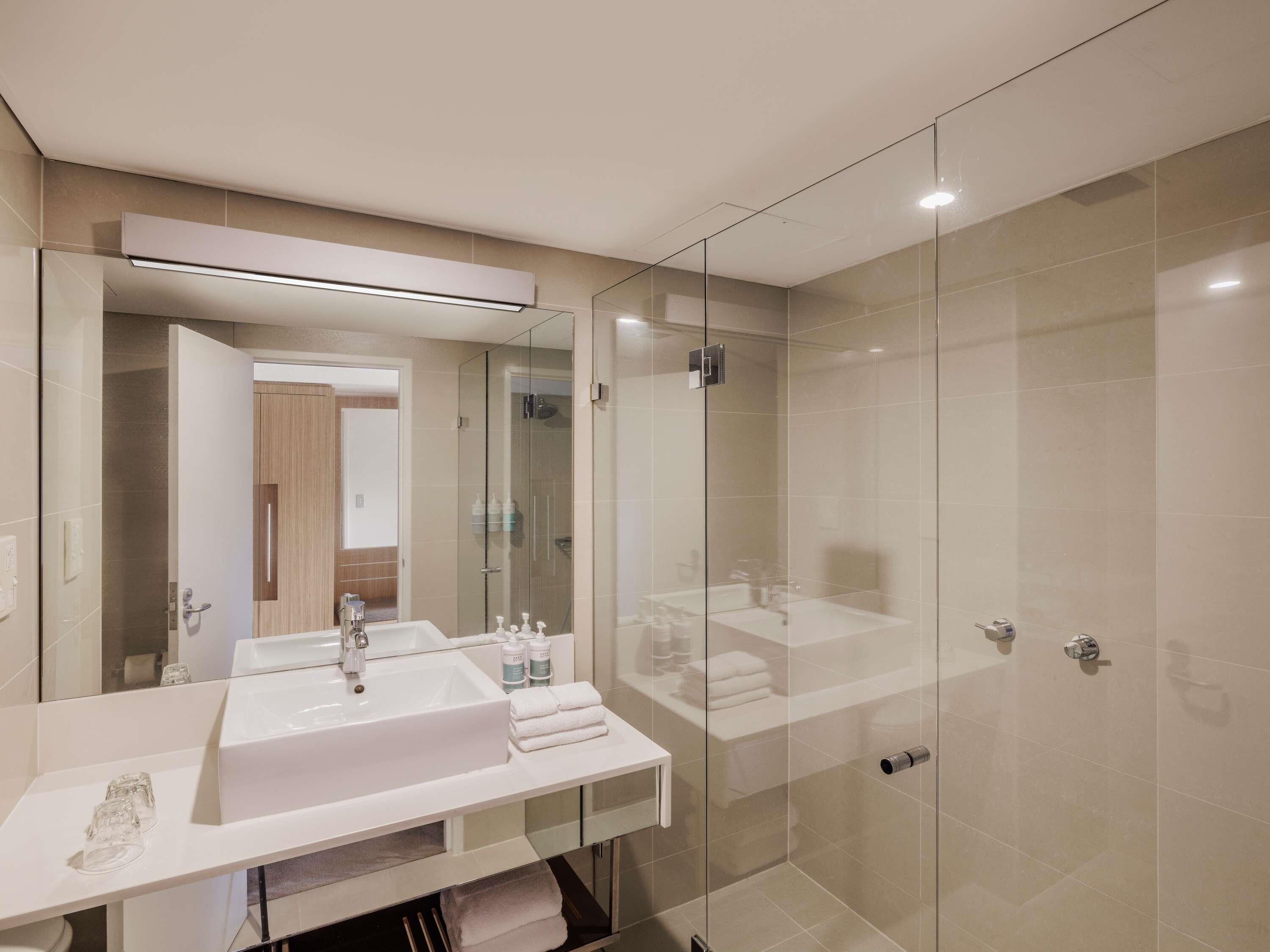 A modern bathroom with a large mirror, a white sink, and a glass-enclosed shower area.