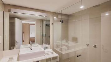 A modern bathroom with a large mirror, a white sink, and a glass-enclosed shower area.