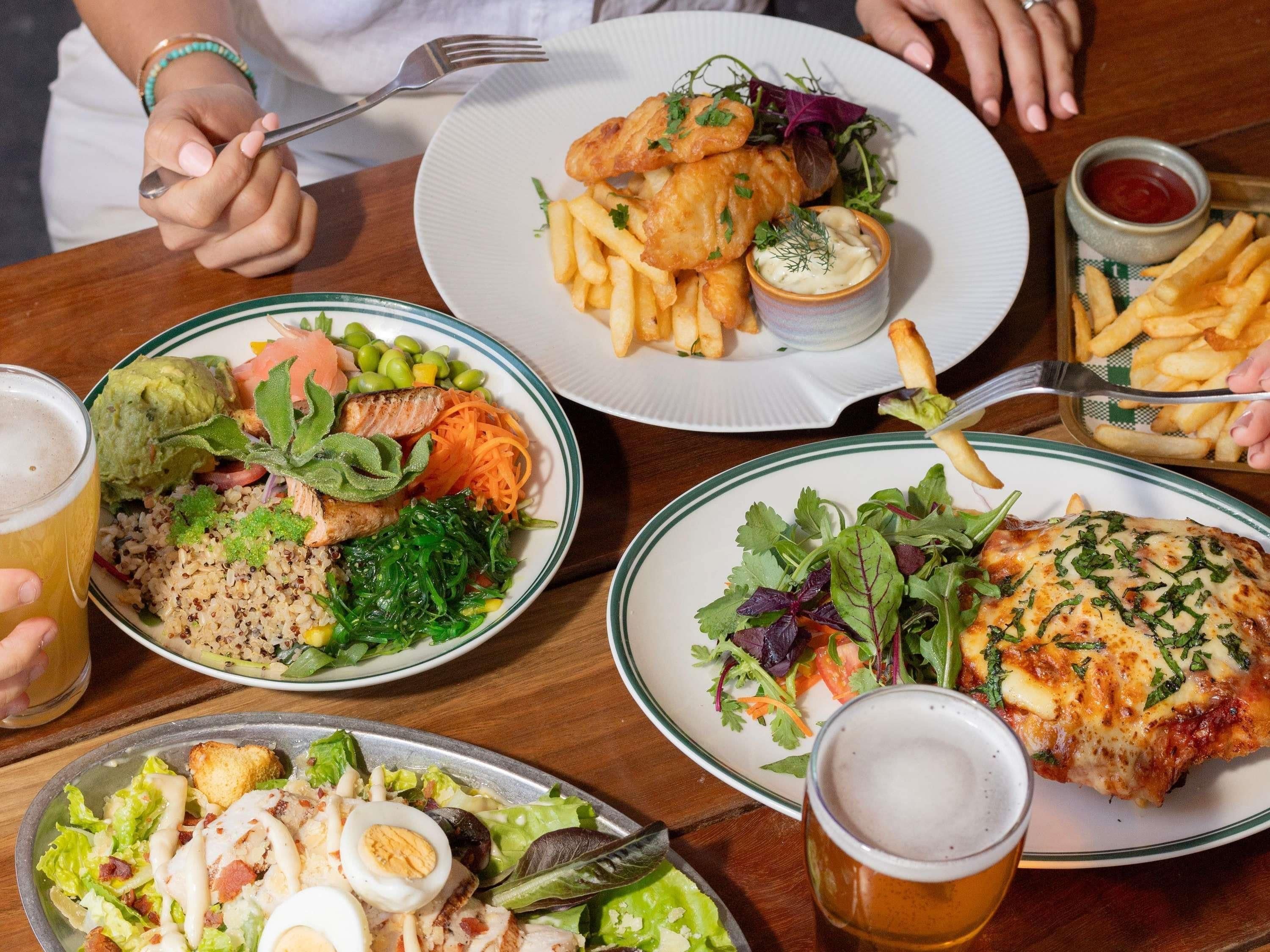 A variety of dishes including fish, salad, and pasta, served on plates with drinks and condiments.