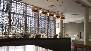 A modern bar area with a geometric patterned wall, multiple hanging spherical lights, and a bar counter with various bottles.