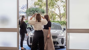 A view through a glass door of a car dealership with a silver car on display.