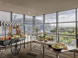 Un comedor moderno con amplios ventanales, un carrito de comida y vistas al Accor Stadium.