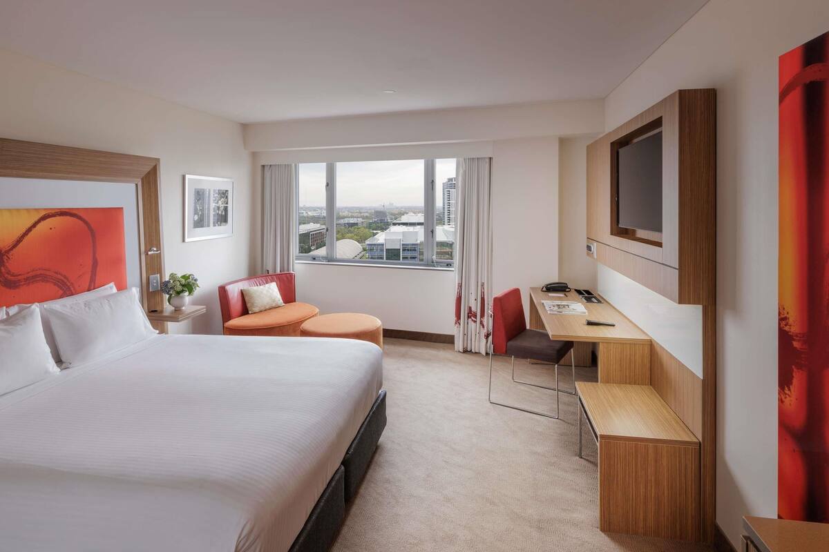 Habitación de hotel con cama, escritorio, silla, televisor y ventana con vista a la ciudad.