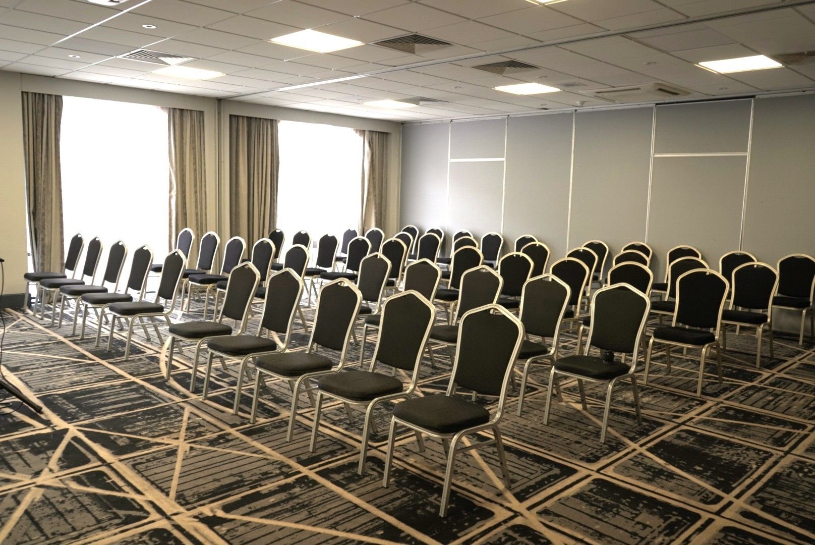 A conference room with rows of chairs, a carpeted floor, and a large window with curtains.