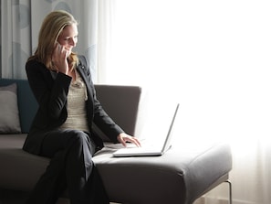 A person sitting on a grey sofa with a laptop, in a room with patterned curtains and a modern design.