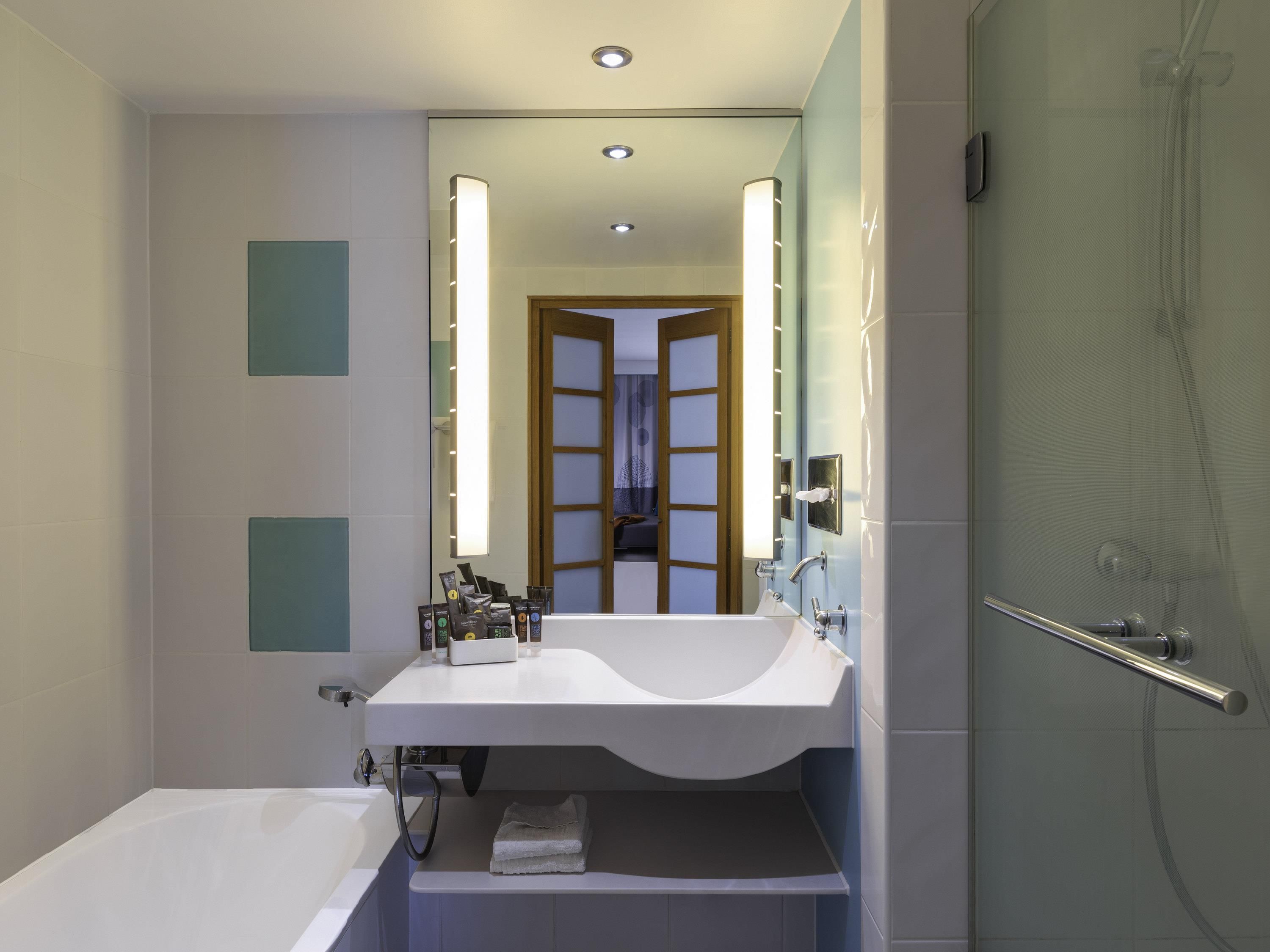 Un baño moderno con lavamanos blanco, espejo y ducha con mampara de vidrio.