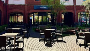 A hotel with a brick facade, multiple windows, and outdoor seating area with tables and chairs. - Novotel Ipswich (Ipswich)