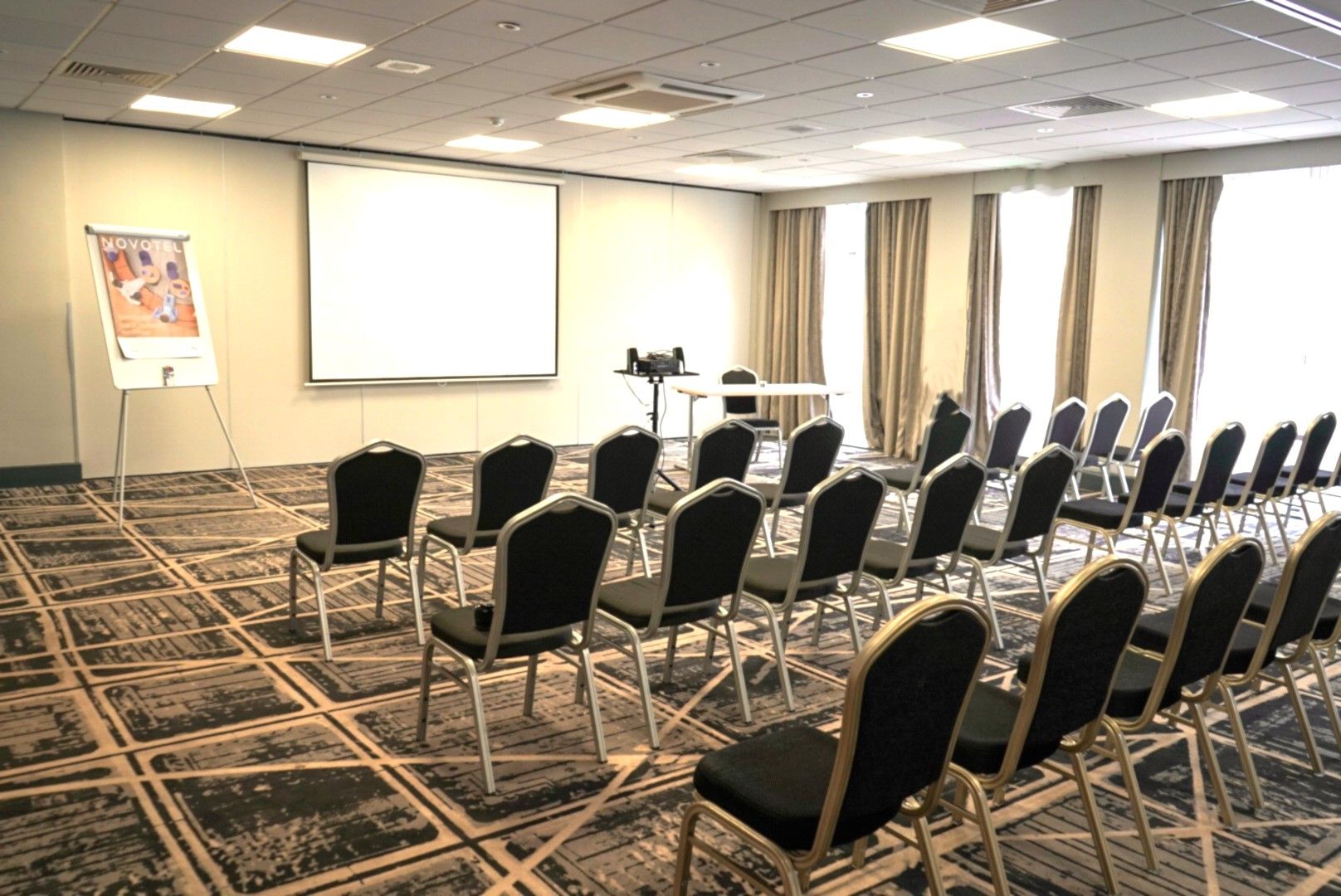Un salón de conferencias con filas de sillas, una pantalla de proyector y un atril.