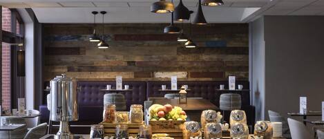 A restaurant with a wooden wall, hanging pendant lights, and a buffet table with fruits and jars.