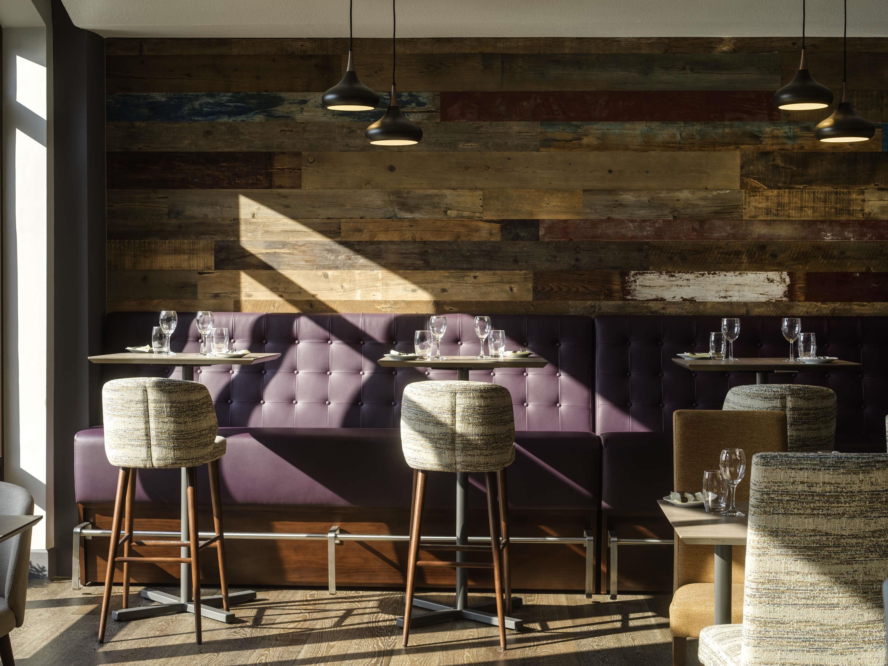 A restaurant interior with a wooden wall, purple seating, and pendant lighting.