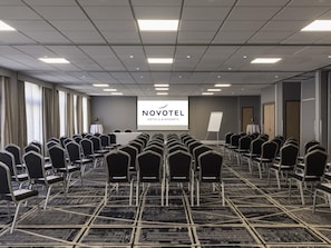 A conference room with rows of chairs, a presentation screen, and a carpeted floor.