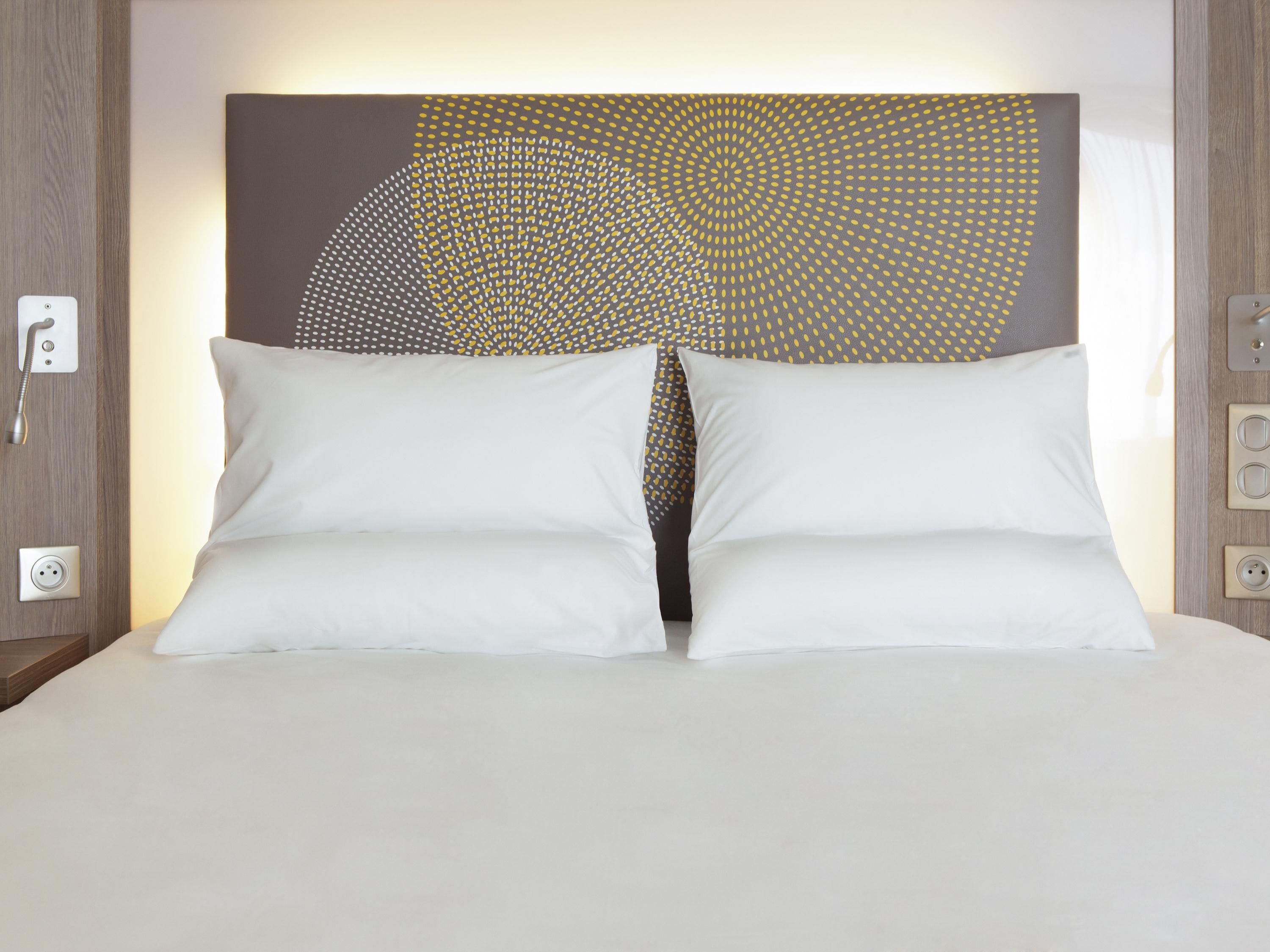 Een bed met witte kussens en een hoofdbord met een geometrisch patroon.