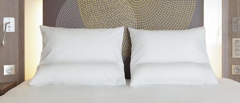 Una cama con almohadas blancas y un cabecero con diseño geométrico.