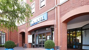 A hotel entrance with a prominent sign, a brick facade, and two large planters.