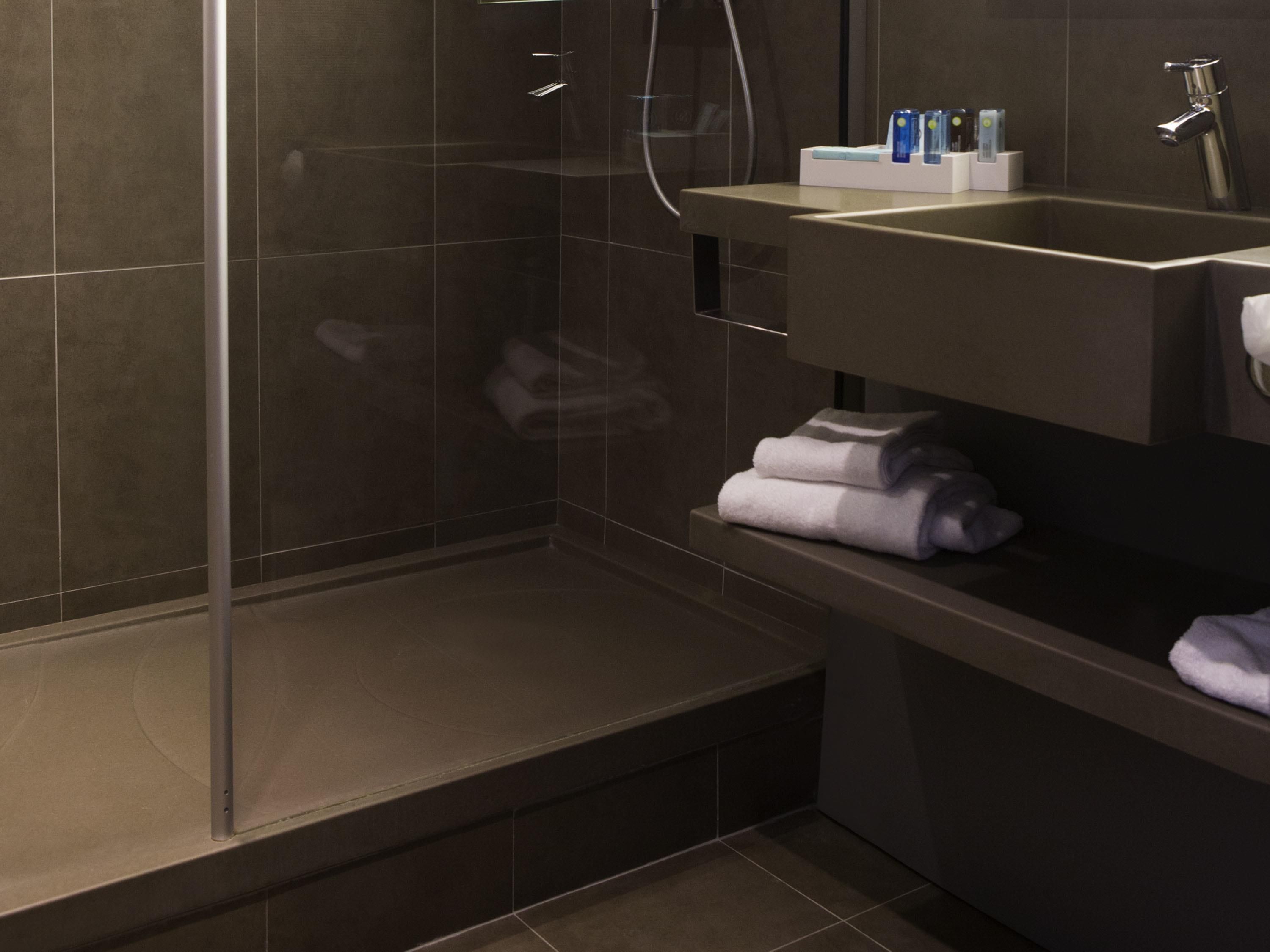 A modern bathroom with a glass shower enclosure, a sink with toiletries, and neatly folded towels.