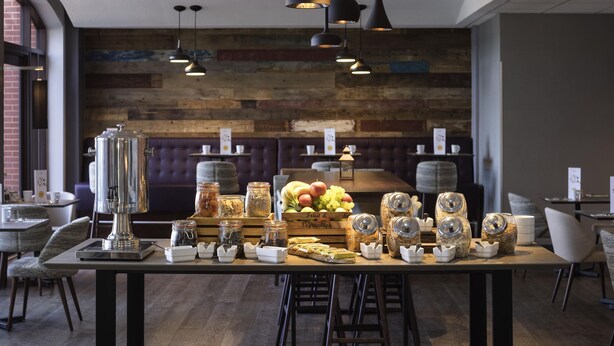 A restaurant with a wooden wall, hanging pendant lights, and a buffet table with fruits and jars. - Novotel Ipswich (Ipswich)
