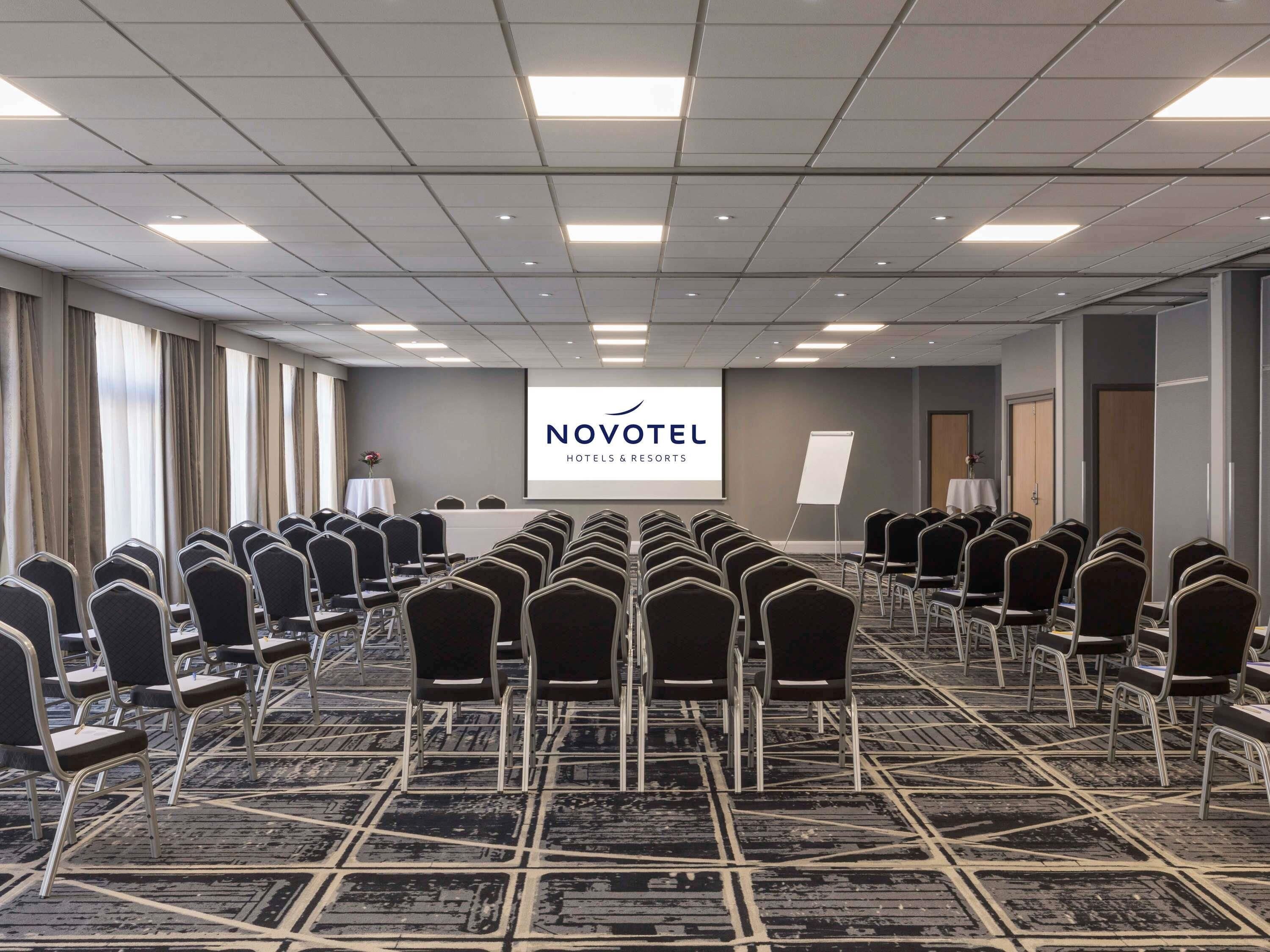 A conference room with rows of chairs, a presentation screen, and a carpeted floor.
