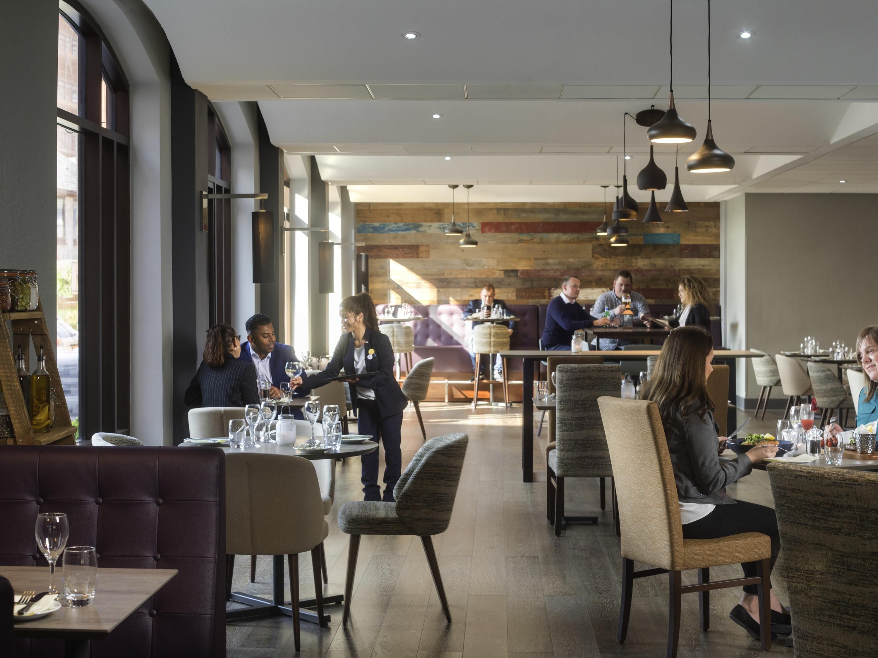 A modern restaurant with high ceilings, large windows, and a mix of seating arrangements including booths and tables.