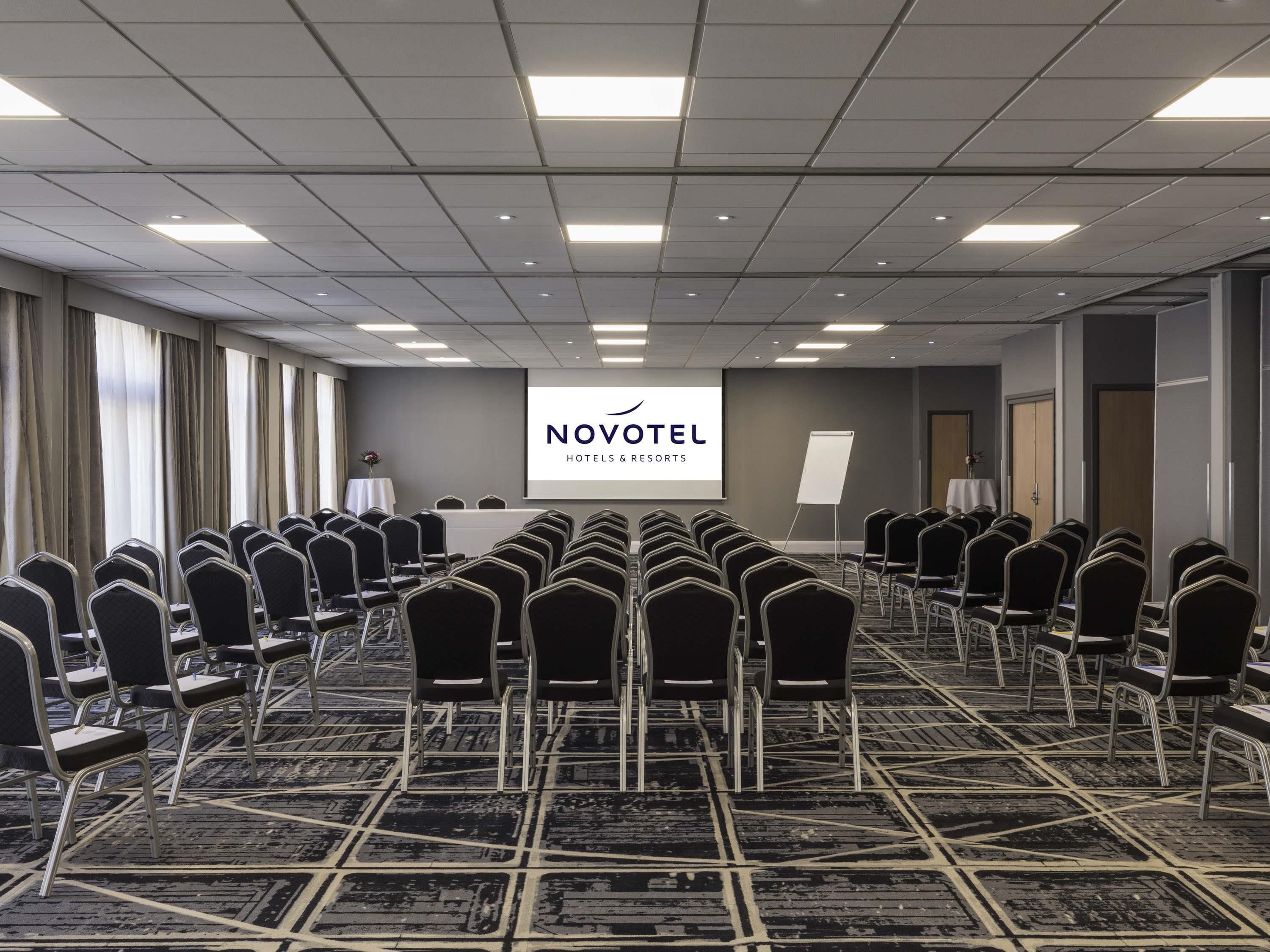 A conference room with rows of chairs, a presentation screen, and a carpeted floor.
