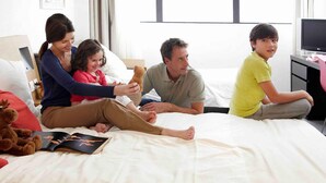 A family sitting on a bed in a hotel room with a television and a desk. - Novotel Ipswich (Ipswich)