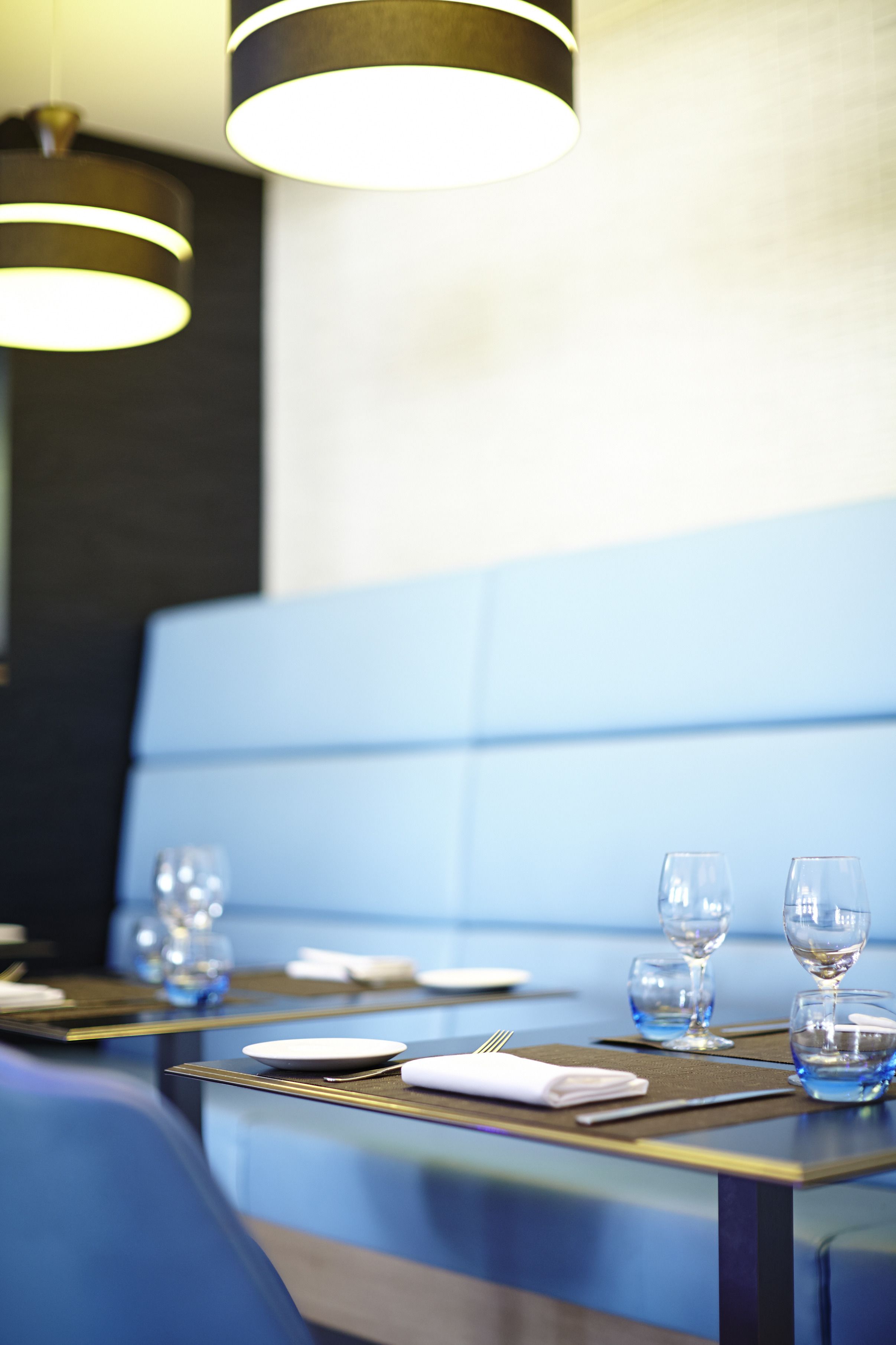 A dining area with a blue cushioned bench, a table set with plates, glasses, and cutlery.