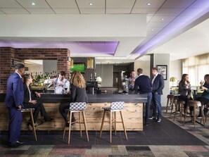 A bar area with stools, a counter, and a television screen displaying a sports game. - Novotel Ipswich (Ipswich)