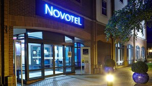 The exterior of a Novotel hotel with automatic doors, a well-lit entrance, and a brick facade. - Novotel Ipswich (Ipswich)