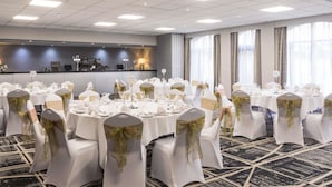A conference room with round tables, white chairs with gold sashes, a bar area, and large windows.